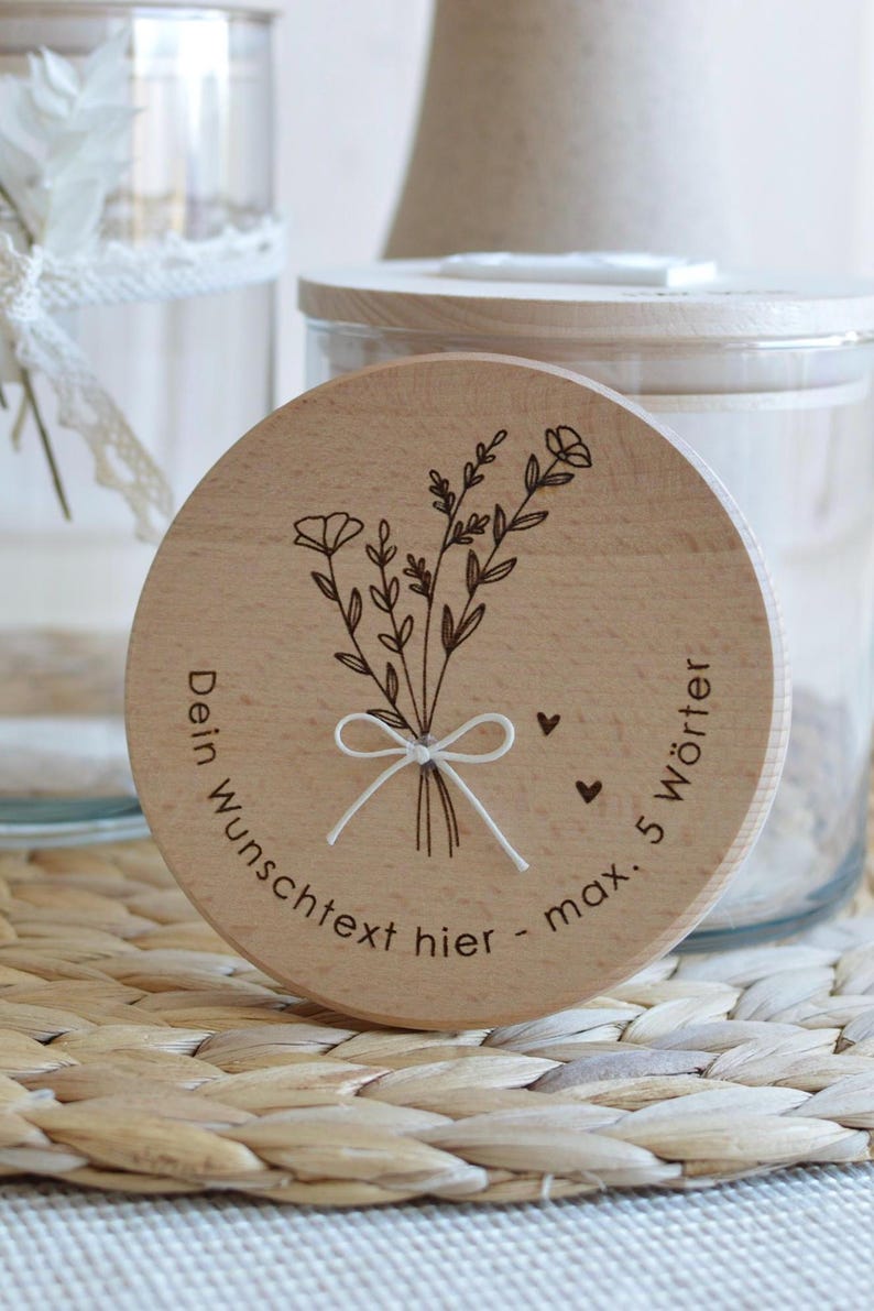 May include: A wooden round jar lid with a floral design and the text "Dein Wunschtext hier - max. 5 W&ouml;rter" engraved on it.