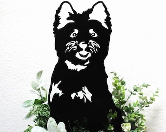 May include: Black metal silhouette of a dog sitting in a planter with green and gray plants and pink flowers.
