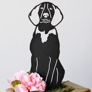 May include: Black silhouette of a dog sitting on a gold cake stand with pink flowers and green moss.