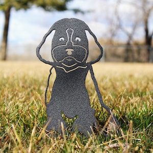 May include: A black metal silhouette of a dog sitting in a grassy field. The dog has a fluffy, curly tail and a friendly expression.
