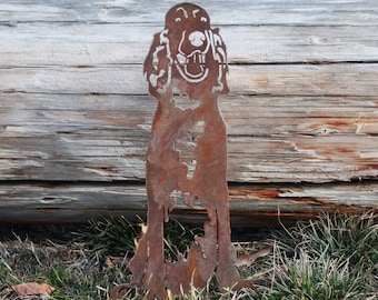 May include: A rusty metal silhouette of a dog standing in front of a weathered wooden log. The dog's head is facing forward with its mouth open and tongue sticking out.
