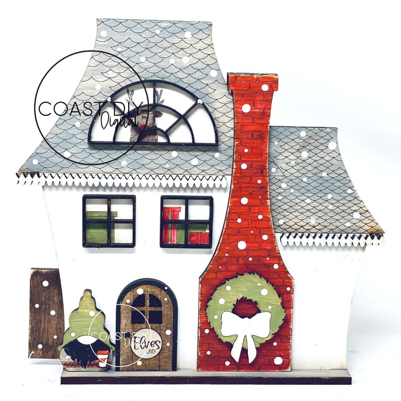 May include: A white wooden Christmas house with a red brick chimney, a green wreath with a white bow, and a sign that reads "Elves Only". The roof is gray with white snowflakes and a window with a reindeer peeking through.