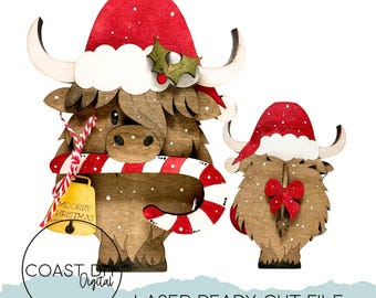Könnte beinhalten: Weihnachtsschmuck aus Holz mit Highland-Rindern. Ein großes Ornament hat einen roten Weihnachtsmannhut, eine Zuckerstange und eine Glocke mit der Aufschrift "Moorry Christmas". Das kleinere Ornament hat eine rote Schleife. Beide haben weiße Hörner und sind mit Schnee bedeckt.