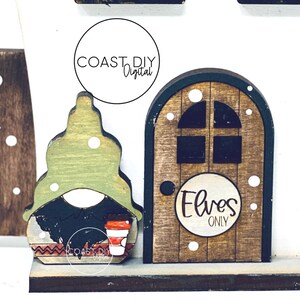 May include: A wooden gnome figurine with a green hat, black beard, and a red cup. The gnome is standing in front of a wooden door with a sign that says "Elves Only".