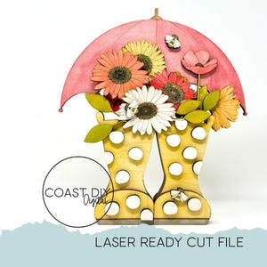 Peut inclure: Pièce d'art en bois découpée au laser représentant des bottes de pluie jaunes à pois remplies de fleurs colorées sous un parapluie rose. Le design comprend des marguerites, des abeilles et le texte "LASER READY CUT FILE".