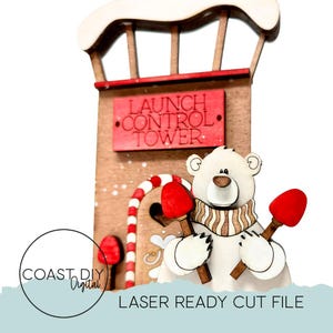 May include: A wooden Christmas ornament featuring a launch control tower with a polar bear holding two red and brown torches. The tower has a red sign that reads "LAUNCH CONTROL TOWER". The ornament has a white and red candy cane door.