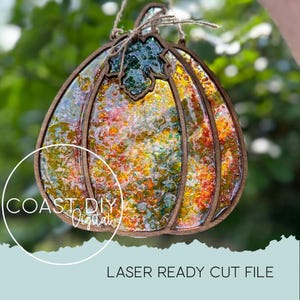 May include: A decorative pumpkin-shaped ornament with a wooden frame and colorful, textured interior. The ornament has a leaf-shaped top and is suspended by a twine string. The text "COAST DIY Digital" and "LASER READY CUT FILE" are visible.