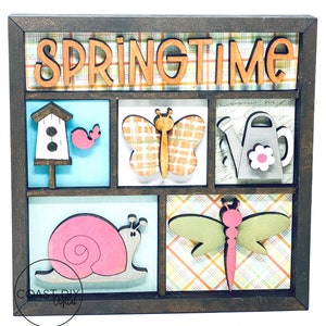 K&ouml;nnte beinhalten: Holz-Wanddekoration zum Thema Fr&uuml;hling mit einem dunkelbraunen Rahmen. Das Wort "SPRINGTIME" steht oben. Das Design umfasst ein Vogelhaus, einen Vogel, einen Schmetterling, eine Gie&szlig;kanne, eine Schnecke und eine Libelle. Der Hintergrund hat ein Karomuster.