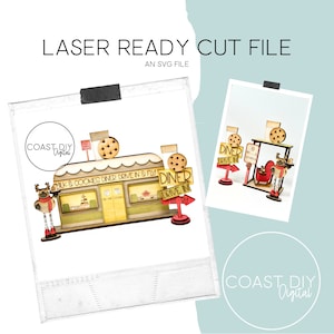May include: Laser cut file design for a milk and cookies diner drive-in. The design features a diner building with a sign that says "Milk & Cookies Diner Drive In & Fly-By", a reindeer, and a sign that says "Diner Drive In".