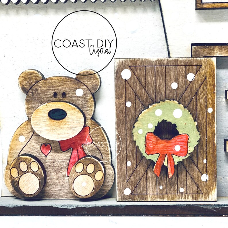 May include: Wooden Christmas decor with a brown bear wearing a red bow and a wooden sign with a green wreath and red bow. The sign has a wood grain pattern and white dots.