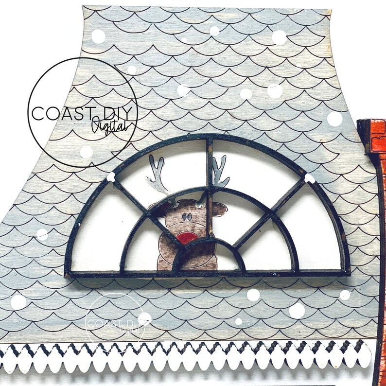 May include: A wooden Christmas house with a reindeer peeking through a window. The roof is decorated with a blue and white pattern and white snowflakes. The house has a white trim and a black and white scalloped edge.