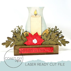 Pode incluir: Centro de mesa de Natal em madeira com uma vela, uma flor de Natal e vegetação. A vela tem uma chama amarela, e a flor de Natal é vermelha com detalhes brancos. A base diz "MERRY & BRIGHT".