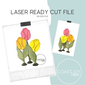 May include: A laser cut file for a three-dimensional tulip bouquet. The bouquet features three tulips, one pink and two yellow, with green leaves and stems. The tulips are arranged in a cluster, with the pink tulip in the center and the yellow tulips on either side. The file is ready to be cut on a laser cutter.