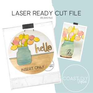 Op de afbeelding: Een houten lasergesneden bestand met een bloemenontwerp. Het ontwerp toont een pot met tulpen in geel, roze en oranje. Het woord "hello" is uitgesneden in een scriptlettertype. De tekst "LASER READY CUT FILE" en "INSERT ONLY" zijn ook zichtbaar.