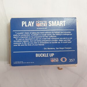 May include: A blue and white card with the text "Play Smart" and "Buckle Up". The card features a quote from Eric Bieniemy, a former San Diego Chargers player, about the importance of wearing a helmet and seatbelt for safety. The card is from the 1992 Pro Set NFL card collection.