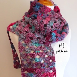 Puede incluir: Una bufanda de ganchillo en tonos de rosa, azul y morado, expuesta en un maniquí blanco. La bufanda tiene un diseño de encaje, abierto. El texto "pdf pattern" es visible en la imagen.