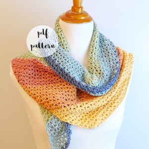 May include: A multi-colored crochet scarf with a light blue, yellow, orange, and red color gradient. The scarf is draped over a white mannequin. The text "pdf pattern" is written in a white circle on the image. The text "fiber flux" is written in a white circle on the image.