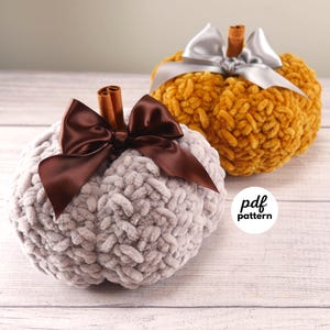 May include: Two plush pumpkins, one gray and one golden yellow, are displayed. Each pumpkin has a cinnamon stick stem and a satin bow. The gray pumpkin has a brown bow, while the yellow pumpkin has a silver bow. A white circle with the text "pdf pattern" is in the lower right corner.