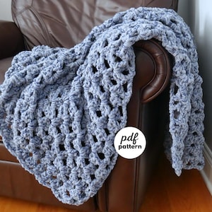 Könnte beinhalten: Eine blaue Häkeldecke mit strukturiertem, offenem Gewebe, drapiert über einem braunen Ledersessel. Das Bild enthält einen weißen Kreis mit dem Text "pdf pattern".