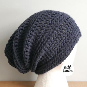 May include: A dark gray crochet beanie hat with a loose, slouchy fit. The hat has a textured, open weave pattern and is displayed on a white mannequin head. The text "pdf pattern" is visible on the lower right side of the image.
