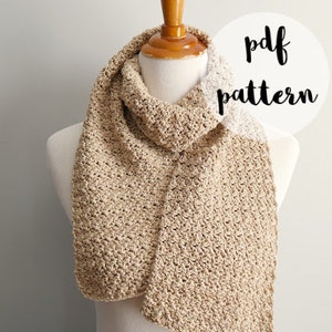 May include: A beige crochet scarf with a textured stitch pattern. The scarf is displayed on a mannequin with a white shirt. The image includes the text "pdf pattern" and "fiber flux".