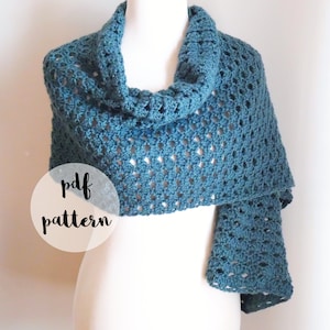 Pode incluir: Um xale de crochê azul turquesa com um padrão rendado. O texto "pdf pattern" está escrito em preto sobre um círculo branco.