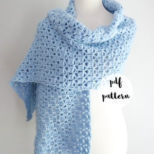 May include: A light blue crochet shawl draped over a wooden mannequin. The shawl has a delicate openwork pattern. The text "pdf pattern" is written in a white circle on the image. The text "fiber flux" is written in a gray circle at the bottom of the image.