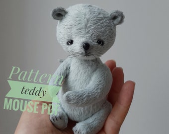 Op de afbeelding: Een grijze pluche teddybeermuis met zwarte ogen en een zwarte neus. De beer zit op een hand.