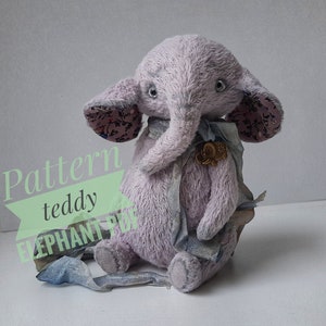 May include: A plush gray elephant teddy bear with floral fabric ears and a blue ribbon around its neck. The bear is sitting on a white surface.