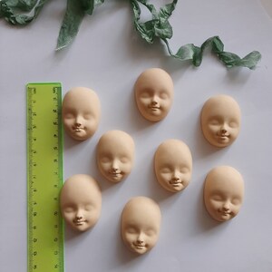 May include: Eight unfinished doll heads made of a light beige clay. The heads are all the same size and shape, and they have a simple, realistic design.