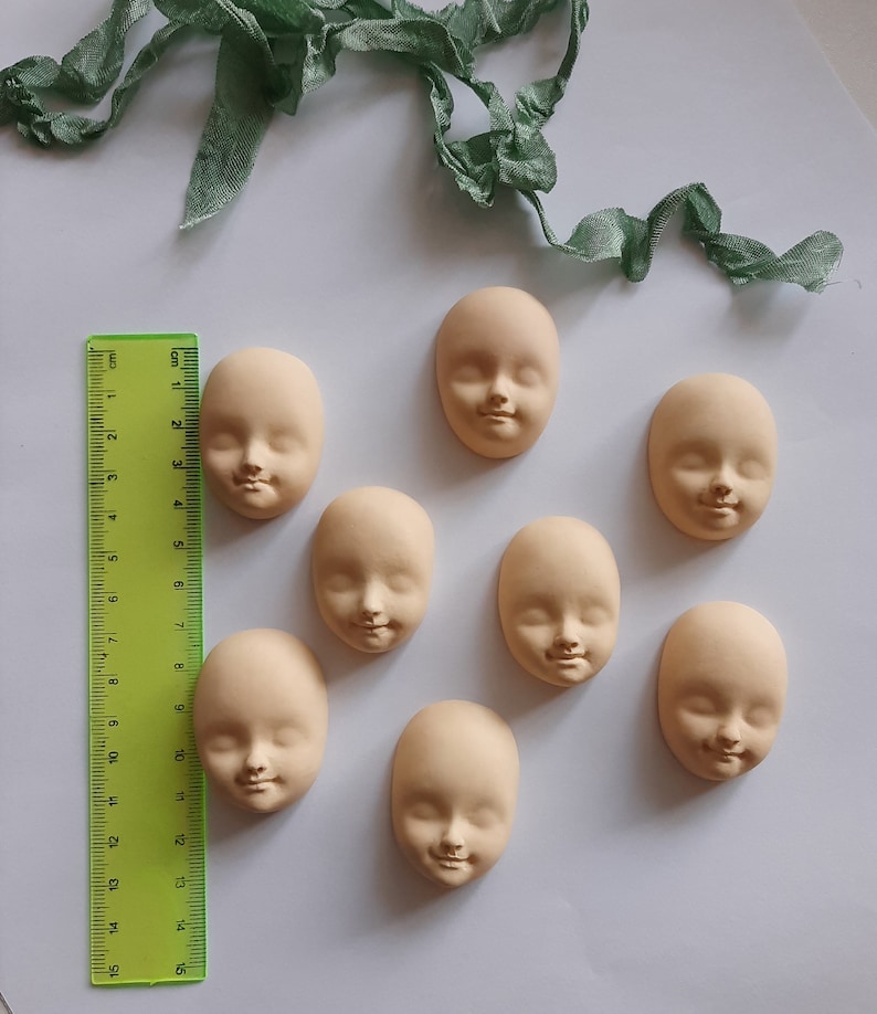May include: Eight unfinished doll heads made of a light beige clay. The heads are all the same size and shape, and they have a simple, realistic design.