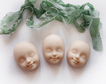 May include: Three unpainted plaster doll heads with closed eyes and neutral expressions. The heads are on a white surface.