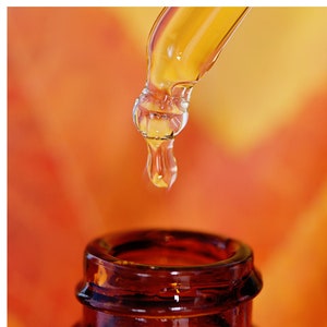 May include: A glass dropper with a clear liquid dripping into a dark brown glass bottle. The background is a blurred orange and yellow.