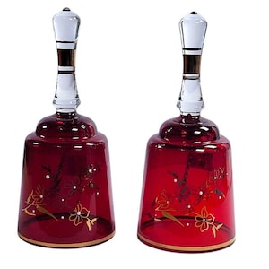 Puede incluir: Dos campanas de cristal rojo rubí con asas de cristal transparente y diseños florales dorados. Las campanas tienen un borde dorado y un badajo de cristal transparente. Las asas tienen un acento dorado y blanco.