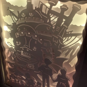 May include: A white papercraft light-up display of a flying airship with two figures standing in front of it. The airship is detailed with windows and a large chimney. The figures are silhouetted against the airship.