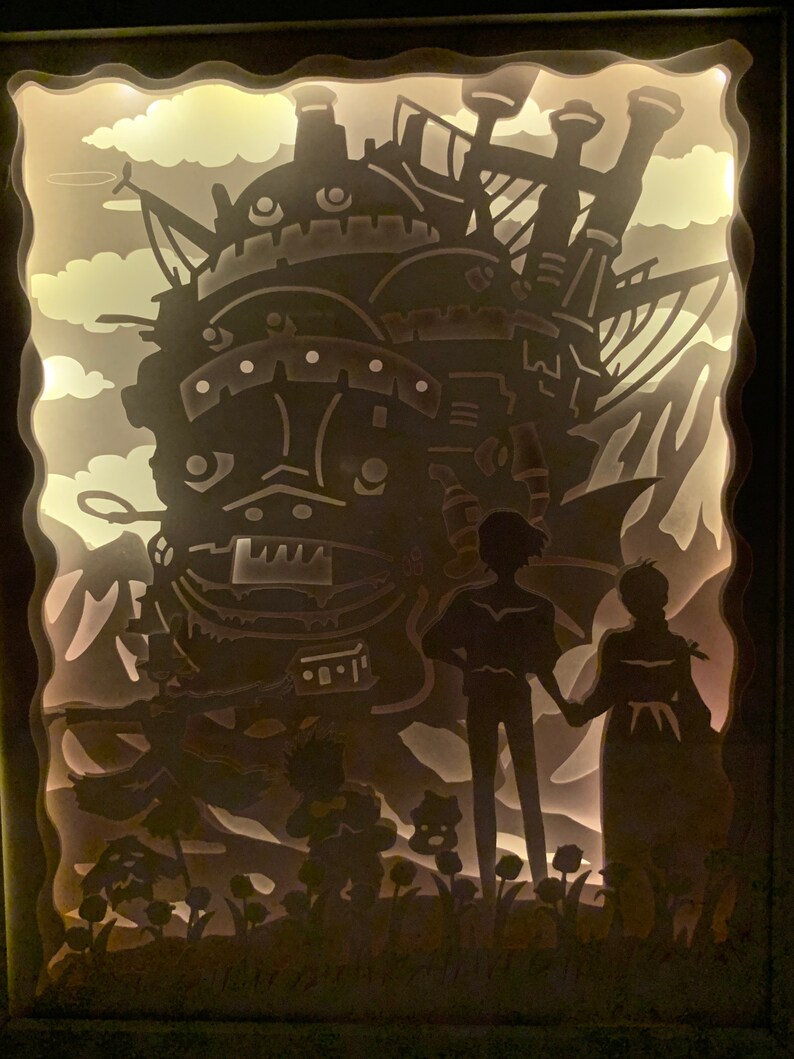 May include: A papercraft light-up display featuring a silhouette of a flying machine from the animated film Howl's Moving Castle. The machine is surrounded by clouds and flowers, and two figures stand in front of it.
