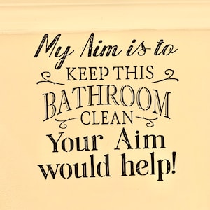 May include: A white bathroom sign with black text that reads "My aim is to keep this bathroom clean. Your aim would help!"