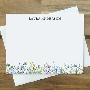 May include: White stationery card with a blue and purple floral border and the name "LAURA ANDERSON" printed at the top.
