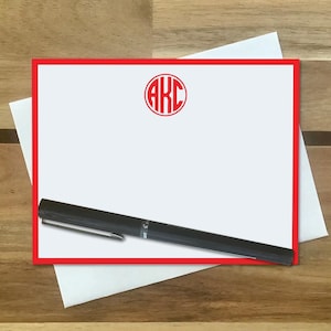 May include: A white card with a red border and a red circle with the letters "AKC" in the center. A black pen is lying on top of the card.