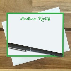 May include: A white card with a green border and the name "Andrew Kurtz" printed in green cursive. A black pen is lying on the card.
