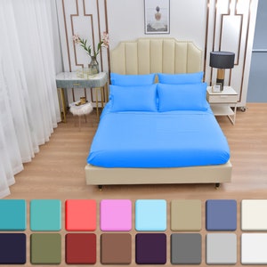 May include: A light blue bed sheet set with a white headboard and a white nightstand with a lamp. The bed is in a bedroom with white walls and a white curtain.