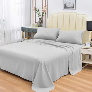 May include: A light gray bed sheet set with two pillowcases. The bed is made with a light gray headboard and a white wall behind it.