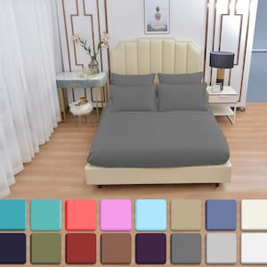 May include: A gray bed with a light beige headboard and a set of gray pillowcases. The bed is in a bedroom with white curtains and a wooden floor. The image also shows a variety of color swatches for the bed linens.
