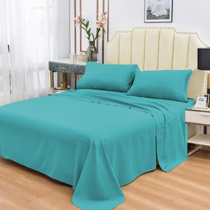 May include: A teal blue bed sheet set with two pillowcases. The bed sheet is on a bed with a white headboard.