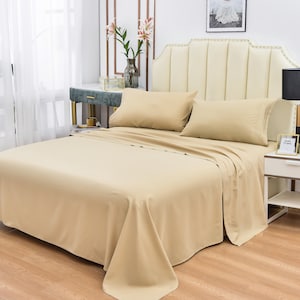 May include: A tan colored bed sheet set with a fitted sheet, flat sheet, and two pillowcases. The bed is made with a white headboard and the sheets are smooth and wrinkle-free.