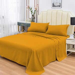 May include: A mustard yellow bed sheet set with two matching pillowcases. The bed is made with a white headboard and the sheet is tucked in neatly.