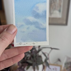 Pu&ograve; includere: Un piccolo acquerello di un cielo blu con nuvole bianche. L'opera d'arte &egrave; firmata e datata "JD.26" con la parola "sky" scritta sotto. Il dipinto &egrave; tenuto in una mano.