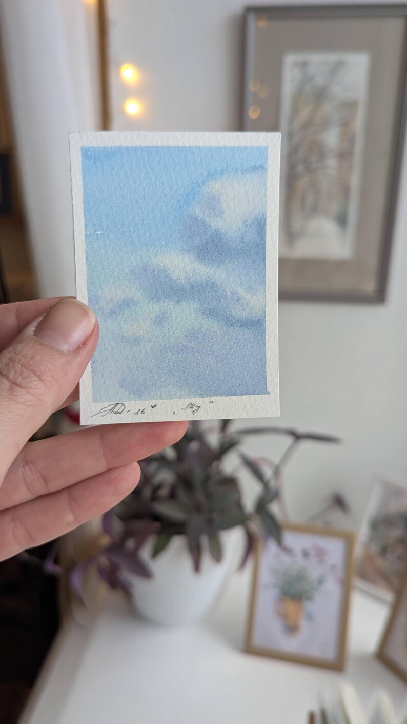 Pu&ograve; includere: Un piccolo acquerello di un cielo blu con nuvole bianche. L'opera d'arte &egrave; firmata e datata "JD.26" con la parola "sky" scritta sotto. Il dipinto &egrave; tenuto in una mano.