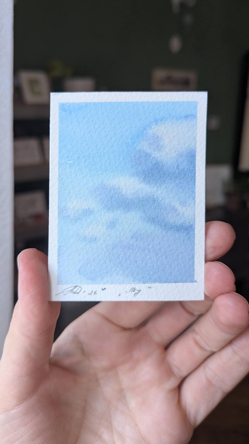 Pu&ograve; includere: Un piccolo acquerello di un cielo blu con nuvole bianche. L'opera d'arte &egrave; su un pezzo di carta rettangolare con un bordo bianco. La firma e la data dell'artista sono nell'angolo in basso a sinistra.