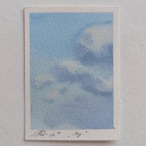 Pu&ograve; includere: Un piccolo acquerello di un cielo nuvoloso. L'opera presenta uno sfondo azzurro chiaro con nuvole bianche e grigie. La firma dell'artista e la data "AD 26" sono visibili nell'angolo in basso a sinistra.